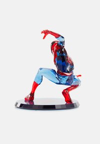 Genomskinlig röd och blå figur i en dynamisk pose, med vinklade fasetter, en blank yta och en rund, mörk bas.