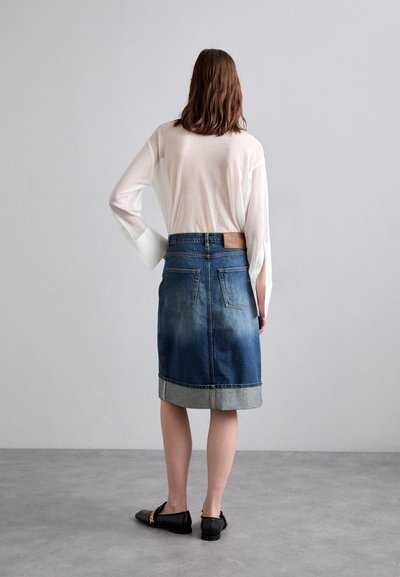 Denimu svārki ar gaismas un tumšas zilas krāsas gradientu, apakšējā mala apdarināta ar gaišāku denimu. Izgatavoti ar brūnu ādas plāksnīti aizmugurē un ar ikdienišķiem melniem apaviem.