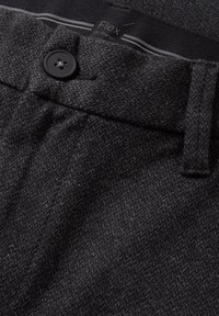 Šedá texturovaná tkanina s vzorem rybí kosti, obsahující černý knoflíkový uzávěr a štítek s nápisem "Flex na cestách" uvnitř pasu.