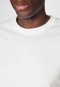 Weißes Baumwoll-T-Shirt mit rundem Ausschnitt und glatter Textur. Nahaufnahme, die den Kragen und den oberen Stoff hervorhebt.