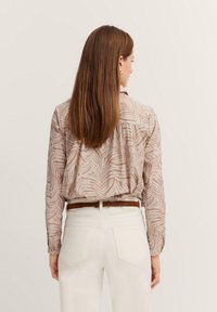 Long-sleeve, light brown blouse with a leaf pattern; paired with white jeans and a brown belt. Back view shows shoulder details and fit.