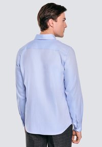 Jasnoniebieska koszula z długim rękawem i kołnierzykiem, z subtelnym wzorem teksturowym. Widoczne zapinane mankiety. Model pokazany z tyłu.