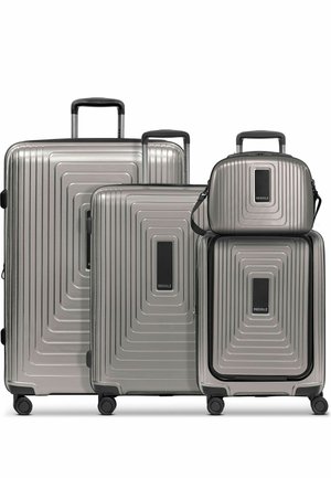 Cuatro maletas rígidas plateadas con asas telescópicas y ruedas, de tamaño variable de grande a pequeño, con etiquetas de marca negras centradas.
