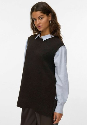 Maglione senza maniche di colore marrone scuro, realizzato in materiale a maglia, con scollo rotondo e leggere aperture laterali, indossato sopra una camicia colloghe blu chiaro.