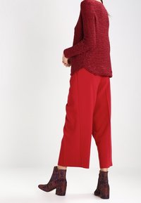 Maglione rosso a textured con maniche lunghe, abbinato a pantaloni rossi a gamba larga e stivaletti con motivo. L'insieme presenta una vestibilità comoda.