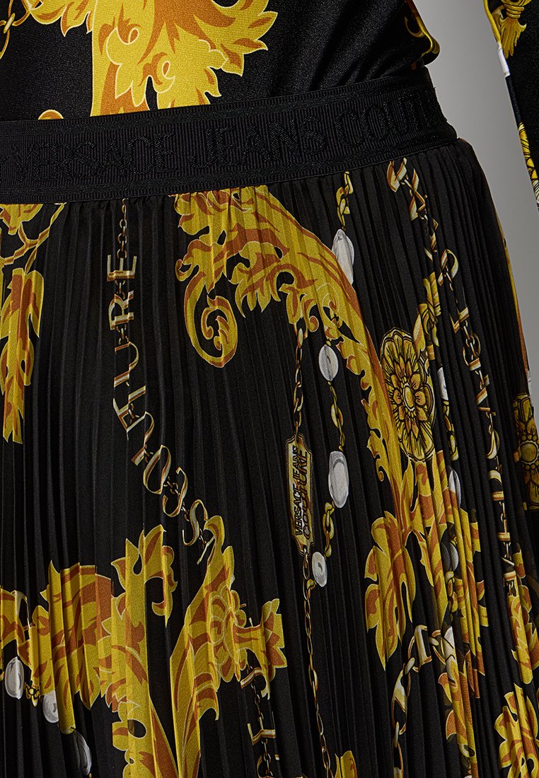 Gonna nera a pieghe con stampa barocca dorata. Presenta un cinturino elastico con il marchio "Versace Jeans Couture". Texture liscia e colori vivaci.