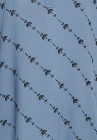Tecido azul com uma textura suave, apresentando um padrão diagonal de motivos florais pretos espaçados uniformemente pela superfície.