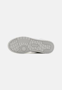 Semelle de sneaker Lacoste en caoutchouc gris ; présente un motif de semelle avec des sections texturisées et un logo central. Design épuré et minimaliste.
