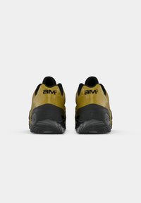 Μαύρα και ελιά-πράσινα αθλητικά παπούτσια με υφασμένη καουτσούκ σόλα, στρογγυλεμένο σχέδιο και εξέχον λογότυπο "am" στη φτέρνα.