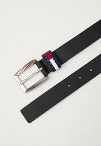 Cinturón de cuero negro con una hebilla rectangular de plata. Presenta un acento de marca en navy, rojo y blanco cerca de la hebilla. Textura suave.