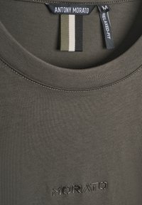 Close-up van de kraag van een olijfgroene, ontspannen pasvorm shirt met een merklabel van "ANTONY MORATO" en een ingedrukte "MORATO" logo op de stof.