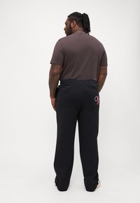 Black sweatpants with an elastic waistband and two back pockets, featuring a subtle design detail in pink on the right pocket.