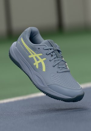 Jasnoszara, sportowa buty z teksturowaną cholewką, żółtymi akcentami i wielokierunkową gumową podeszwą, zaprojektowane z myślą o wydajności na boiskach.