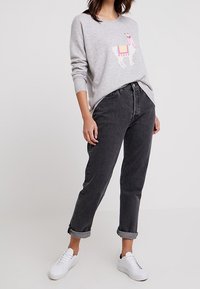 Pull gris avec un imprimé lama, associé à un jean noir taille haute, ourlets retroussés, et des baskets blanches. Texture lisse, coupe décontractée.