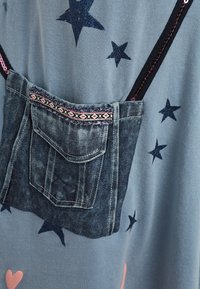 Niebieska tkanina z ciemnoniebieskimi wzorami gwiazdek. Zawiera dżinsową kieszeń z dekoracyjnym różowym i czarnym wykończeniem, przymocowaną czarnymi paskami.