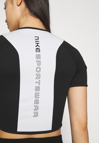 Musta-valkoinen lyhythihainen urheilupaita, jossa on näyttävä "NIKE SPORTSWEAR" -logo selässä paksuilla kirjaimilla.