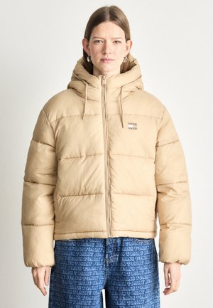 Beige pufferjacka med huva, framdragkedja och dragsko. Har ett subtilt rutmönster och metall-logotypdetaljer.