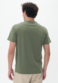 Tricou scurt din bumbac de culoare verde măsliniu, fabricat dintr-un material moale, cu guler rotund și un design simplu, fără logo-uri sau modele vizibile.