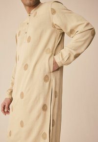 Beige Kurta mit goldenen Paisley-Stickereien, langen Ärmeln, knopfbedecktem Ausschnitt, seitlichen Schlitzen und einer lockeren Passform. Leichter Stoff.