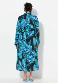 Lång svart klänning med livfullt blått och grönt bladmönster, med långa ärmar och midjebälte. Bärs med blå klacksandaler.