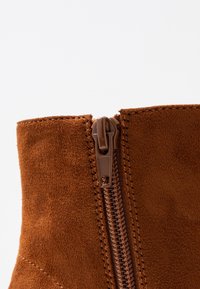 Bruine suède enkellaarzen met een ritssluiting aan de zijkant, voorzien van zichtbare stiksels en een gladde textuur, met een ronde neus en een aansluitende vorm.