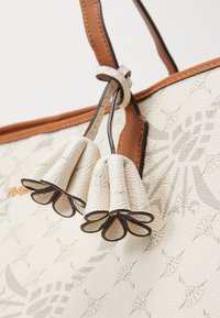 Beige tygväska med strukturerad yta, med bruna läderdetaljer och dekorativa beige läderfransar, med ett subtilt mönster.