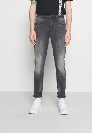 Vaqueros de denim gris con un corte slim, un ligero desgaste y dobladillos acampanados, combinados con una camiseta negra y zapatillas blancas.