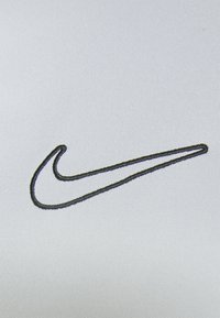 Camiseta Nike con una suave tela gris claro y un logo negro bordado prominente en forma de swoosh.