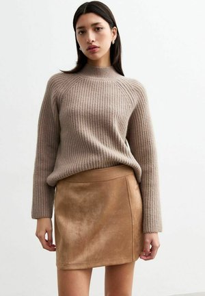 Beige geribde gebreide trui met hoge hals; gecombineerd met een tan suède minirok met naaddetails en een zachte textuur.