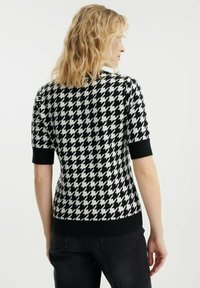 Černobílý svetřík s krátkým rukávem se vzorem houndstooth, s obepínajícím střihem a žebrovanými černými manžetami a spodním lemem.