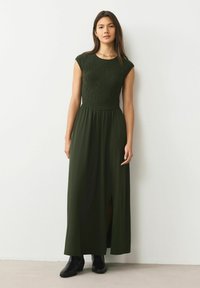 Ciemnozielona sukienka maxi z marszczonym gorsetem, krótkimi rękawami typu cap i przednim rozcięciem. Noszona z czarnymi botkami za kostkę. Gładka, lekka tkanina.