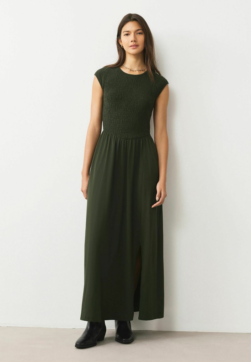 Ciemnozielona sukienka maxi z marszczonym gorsetem, krótkimi rękawami typu cap i przednim rozcięciem. Noszona z czarnymi botkami za kostkę. Gładka, lekka tkanina.