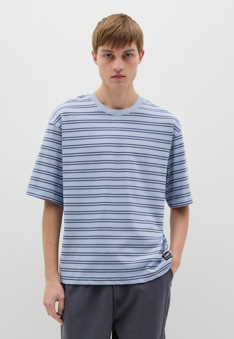 Camiseta de manga corta azul claro con rayas horizontales en navy. Cuello redondo, corte relajado y pequeña etiqueta de la marca en la costura lateral.
