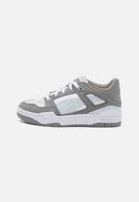 Sneaker bianco e grigio con tomaia in pelle e mesh, suola in gomma, colletto imbottito e accenti in contrasto discreti. Presenta un marchio prominente.