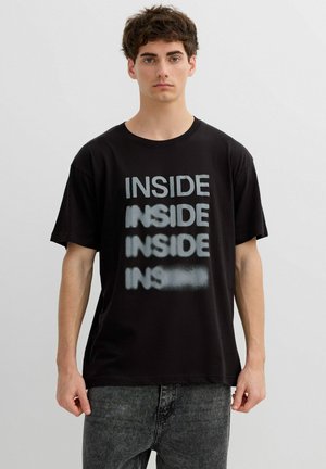 Joven con camiseta negra con la palabra "INSIDE" impresa cuatro veces, desvaneciéndose progresivamente de arriba hacia abajo.