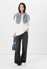 White long-sleeve shirt, gray knitted sweater draped around shoulders, dark wide-leg jeans, white sneakers, and a blue handbag.