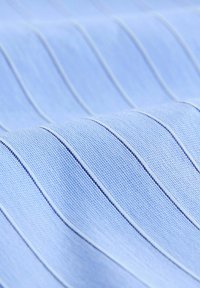 Tessuto azzurro chiaro con un motivo testurizzato a sottili strisce verticali blu scuro. Texture liscia con un disegno intrecciato.