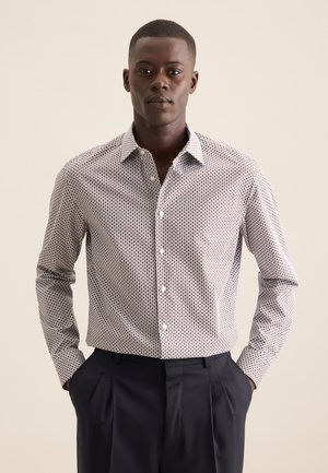 Chemise blanche à boutons avec un motif géométrique rouge et marine, à manches longues et col classique. Associée à un pantalon marine foncé.