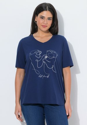 Kobieta z długimi ciemnymi włosami nosi granatowy T-shirt z dekoltem w serek, na którym widnieje rysunek ciągłą linią dwóch zabawnych wydr trzymających się za ręce.