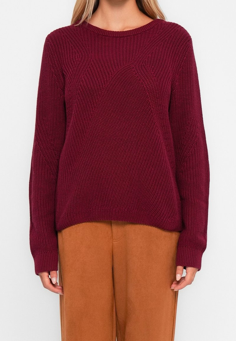 Pull bordeaux avec un motif tricoté texturé, doté d'un col rond et de manches longues, associé à un pantalon en daim marron.