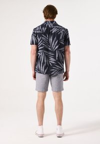 Korte mouwen shirt met een donkerblauw en grijs bladpatroon; gecombineerd met lichtgrijze shorts en witte sneakers, gezien vanuit de achterkant.