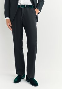 Pantaloni neri eleganti a taglio slim, abbinati a scarpe in velluto verde scuro e una cintura abbinata in velluto. Tessitura liscia e design sartoriale.