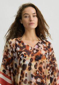 Kaftan astratto in stampa leopardo realizzato in tessuto leggero e trasparente, con scollo a V e accenti a strisce rosse e bianche in contrasto sulle maniche.