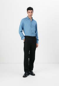 Camicia in denim blu chiaro con bottoni, abbinata a pantaloni neri su misura e scarpe nere. Design semplice, maniche lunghe e vestibilità dritta.