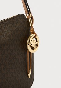 Brown patterned leather handbag with gold hardware, featuring a round logo accent, smooth zipper pull, and a braided shoulder strap.