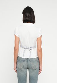 Λευκό πουκάμισο με κοντά μανίκια και γιακά, με ριγέ γραβάτα στη μέση. Συνδυάζεται με μπλε τζιν ψηλόμεσο με τσέπες στην πλάτη.