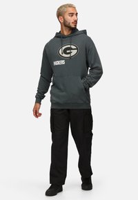 Grå hoodie med "G PACKERS"-logotyp, dragsnören och framficka; matchad med svarta cargobyxor och svarta skor. Avslappnad passform och stil.