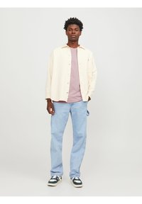 Lysbeige skjorte med knapper over en lilac t-shirt, parret med lyseblå jeans og sort-hvide sneakers. Casual fit, minimale mønstre.