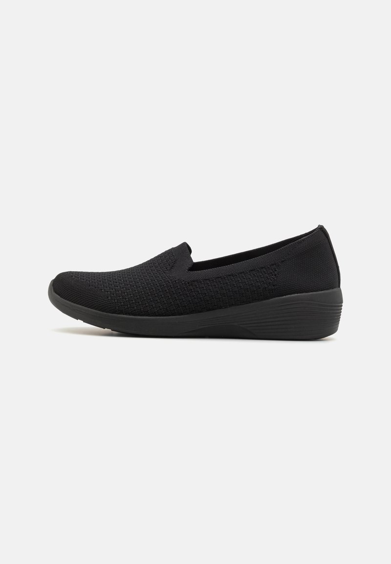 Black slip-on shoe with textured knit upper and slightly raised sole, designed for casual or comfort wear, shown in side profile on white background.