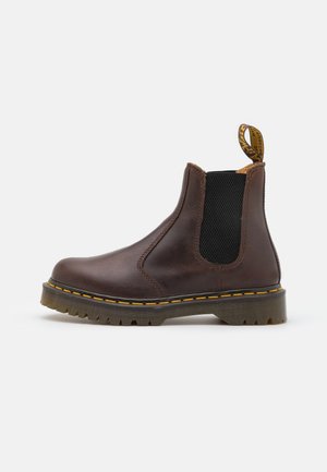 Brauner Chelsea-Stiefel aus Leder mit schwarzem elastischem Seitenpanel, gelber Naht entlang der Sohle und markiertem Zugband hinten.